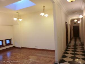 Wnętrze biura w Śródmieściu: przestronny pokój z parkietem, oświetlony lampami wiszącymi i światłem dziennym wpadającym przez okno dachowe, widok na korytarz z czarno-białą szachownicą na podłodze.