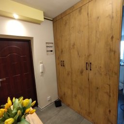 ZDOBRYMSMAKIEM.PL KRZYSZTOF RUTKOWSKI - Drewniana szafa wnękowa z czterema drzwiami, czarne uchwyty, szara podłoga, widok z perspektywy, bukiet tulipanów w wazonie na pierwszym planie.