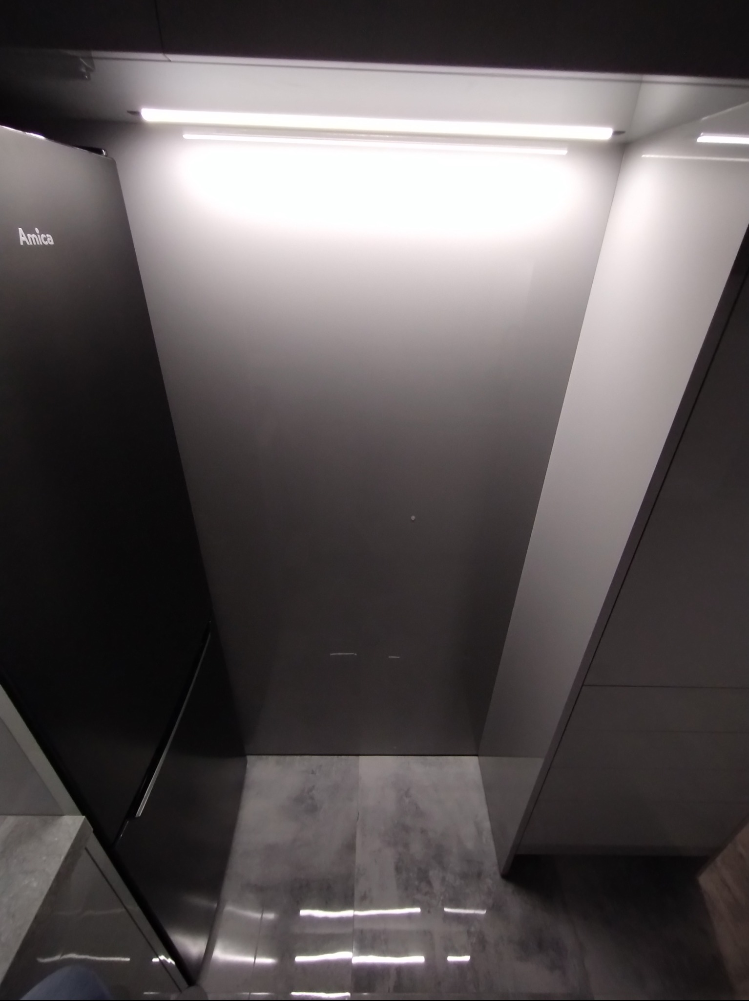 Nowoczesna kuchnia z oświetleniem LED, widok z dołu. Minimalistyczny design, szare fronty szafek, sprzęt AGD marki Amica. Ujęcie podkreśla geometrię i oświetlenie wnętrza.