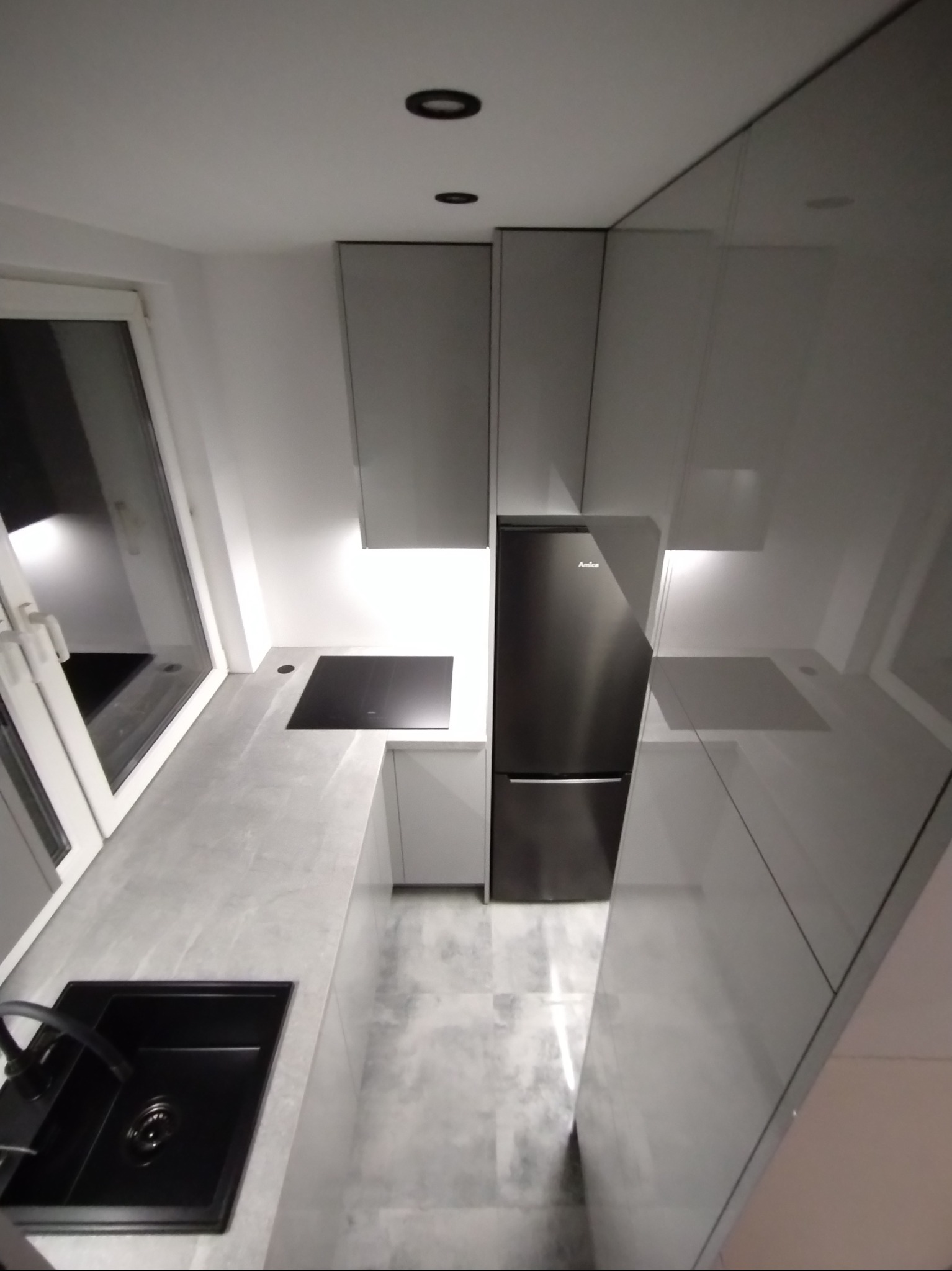 Nowoczesna, szara kuchnia z czarnym zlewem i płytą indukcyjną. Minimalistyczny design, oświetlenie punktowe, widok z góry podkreśla układ zabudowy.