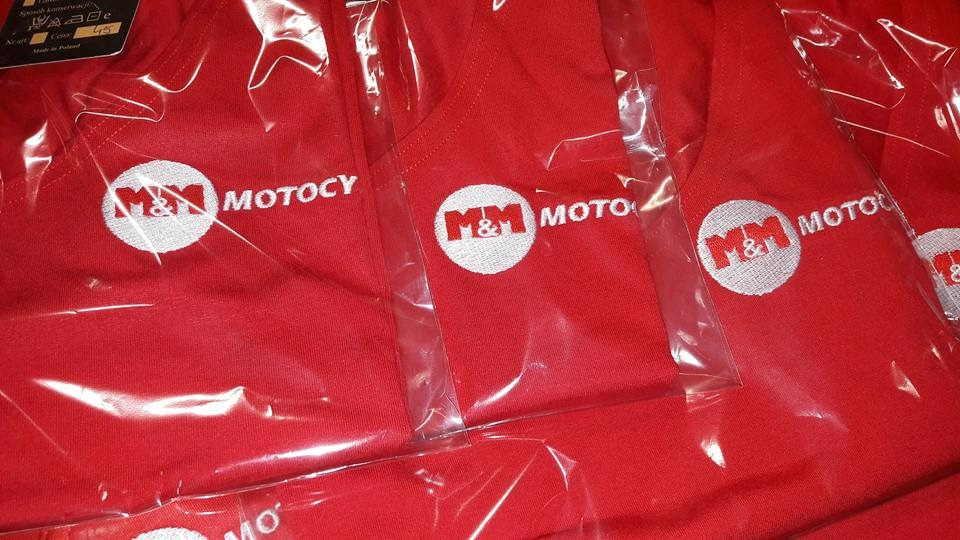 Czerwone koszulki z logo M&M Moto w folii, wykonane metodą haftu. Widoczne detale logo i materiału. Gotowe zamówienie dla klienta.