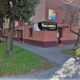 Budynek agencji nieruchomości Domstyl z widocznym logo, otoczony drzewami i chodnikiem z kostki brukowej.