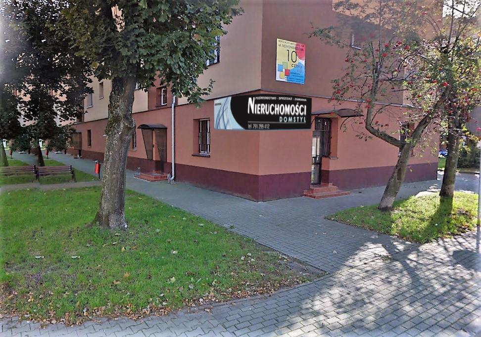 Budynek agencji nieruchomości Domstyl z widocznym logo, otoczony drzewami i chodnikiem z kostki brukowej.