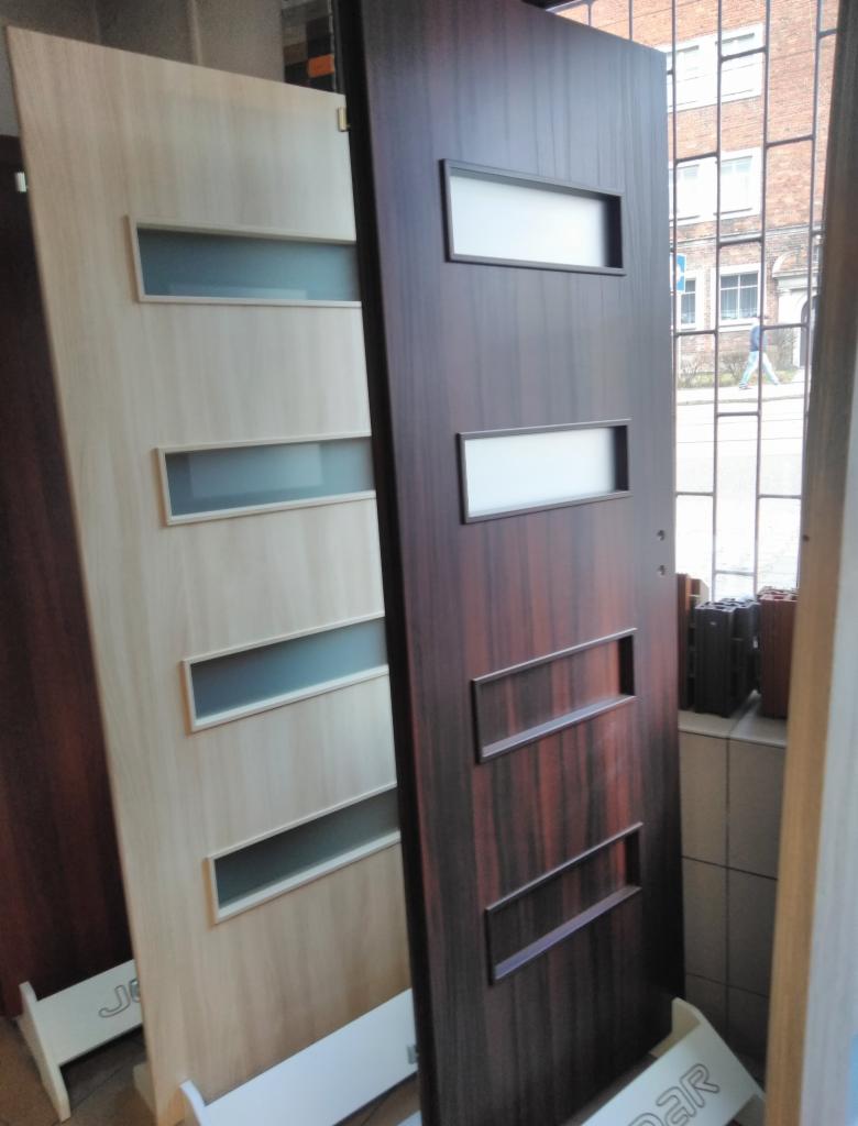 Dwa modele drzwi wewnętrznych: jasne drzwi z czterema przeszkleniami i ciemne drzwi z dwoma przeszkleniami oraz dwoma dekoracyjnymi wgłębieniami.