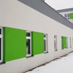 Świeżo pomalowana elewacja budynku z białymi ścianami i jaskrawo zielonymi akcentami wokół okien, widok z zewnątrz w zimowej scenerii.