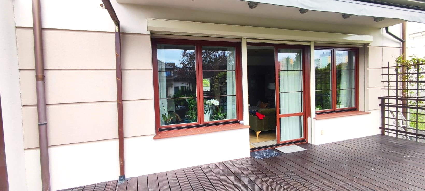 Jasna elewacja domu z drewnianymi oknami i przesuwnymi drzwiami tarasowymi, widok z drewnianego tarasu.