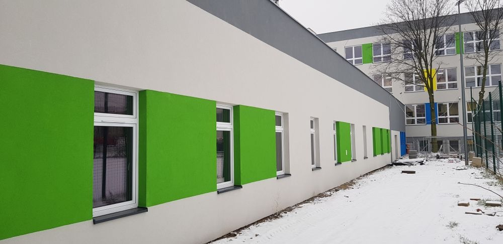 Świeżo pomalowana elewacja budynku z białymi ścianami i jaskrawo zielonymi akcentami wokół okien, widok z zewnątrz w zimowej scenerii.