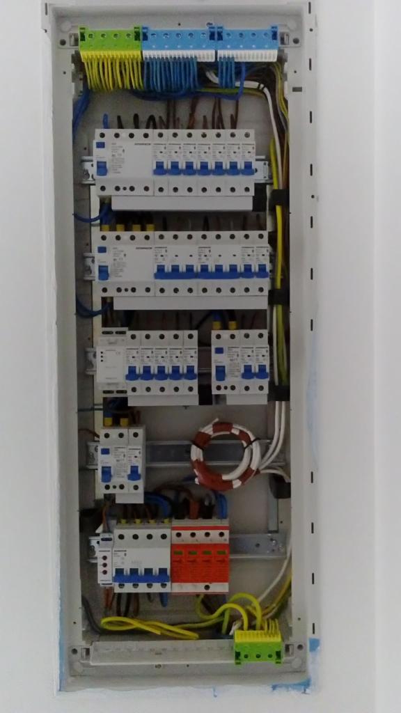 Rozdzielnica elektryczna w obudowie, widoczne bezpieczniki, przewody w różnych kolorach (żółty, niebieski, biały, brązowy), listwy zaciskowe.
