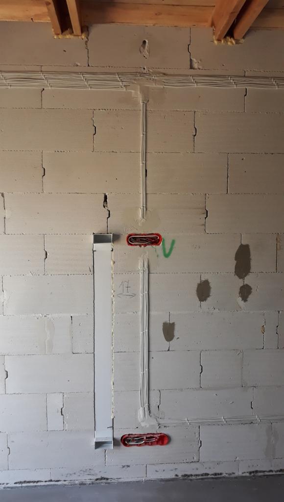 Ściana z betonu komórkowego z widocznymi przewodami elektrycznymi ułożonymi w korytach i puszkach, widoczne ślady po zaprawie i oznaczenia na ścianie.