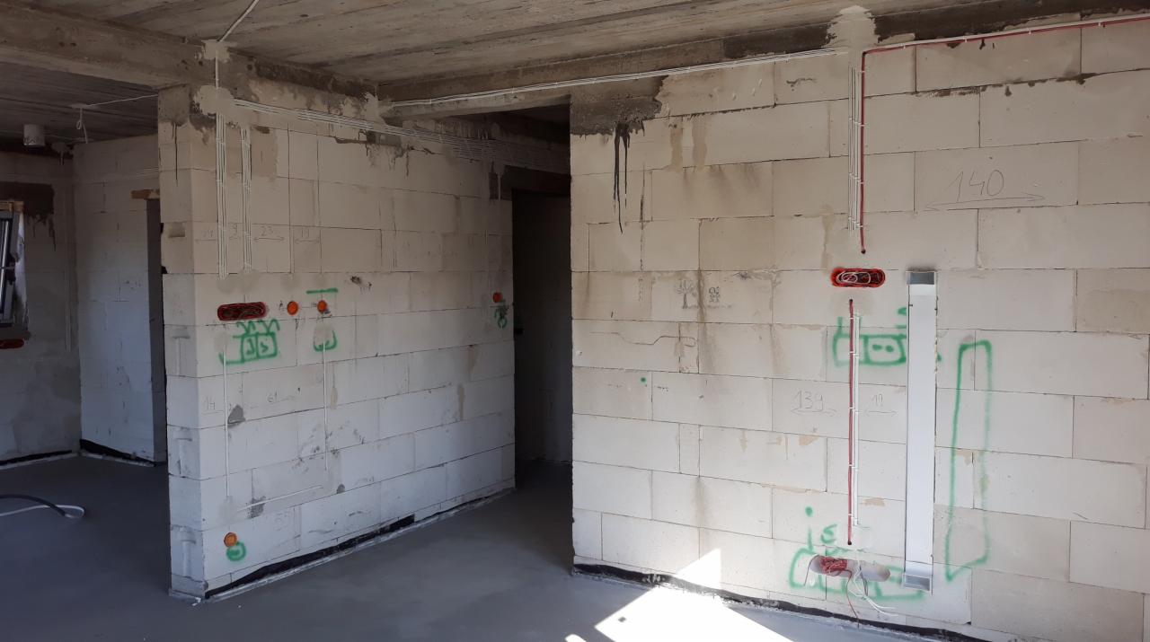 Wewnętrzne ściany budynku w Chęcinach z widocznymi przewodami elektrycznymi w trakcie montażu, oznaczone zielonymi symbolami i numerami. Czerwone kable prowadzone wzdłuż ściany.