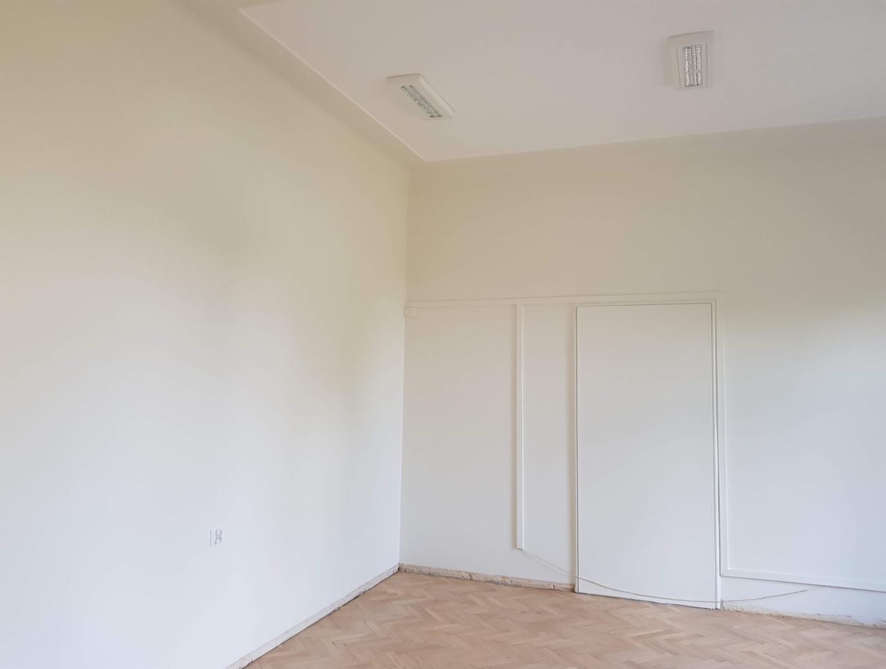 Jasne wnętrze po odświeżeniu, ściany w odcieniach bieli, parkiet ułożony w jodełkę, widoczne ślady po remoncie przy podłodze.