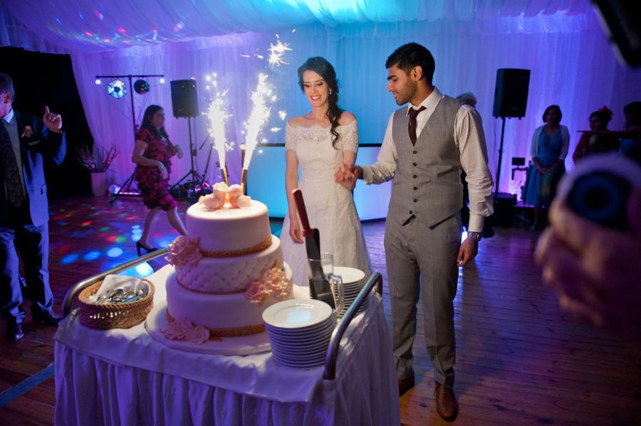 Para młoda kroi tort weselny z fontannami iskier na tle sali z oświetleniem dyskotekowym.