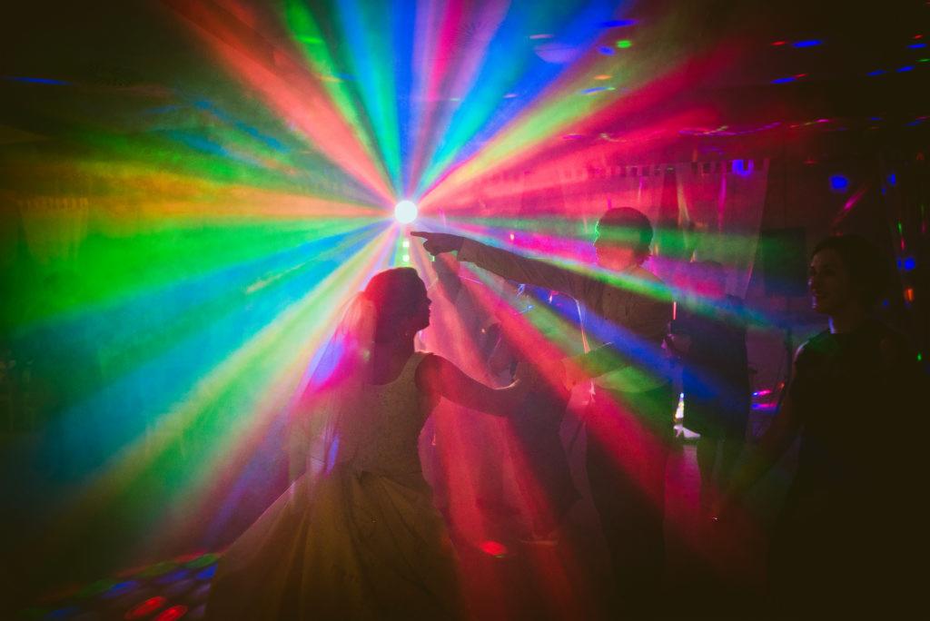 Para młoda tańczy w stroboskopowym oświetleniu podczas wesela, z mężczyzną wskazującym na światło.