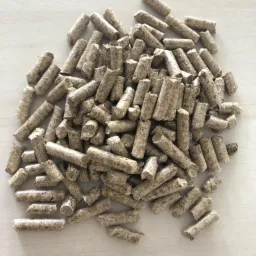 Góra jasnych, brązowo-szarych peletek z widoczną strukturą włókien drzewnych, ułożonych na gładkiej, jasnej powierzchni.