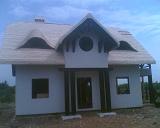 Dom z dachem pokrytym wiórem osikowym, widoczne okna dachowe w kształcie półksiężyca i kolumny podtrzymujące wejście.