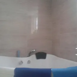 Biała wanna z hydromasażem pod beżowymi płytkami, widok na ścianę z oknem i świecznik na ścianie kabiny prysznicowej.