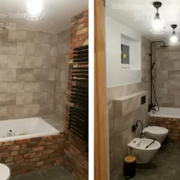 Nowoczesna łazienka z wanną obudowaną czerwoną cegłą, szarą płytką imitującą kamień na ścianach, czarną armaturą i grzejnikiem drabinkowym, oświetlona wiszącymi lampami w stylu industrialnym.