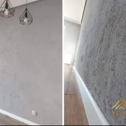 Szara ściana z dekoracyjną fakturą, oświetlona przez dwie nowoczesne lampy wiszące, listwa przypodłogowa, widok z bliska na strukturę ściany.