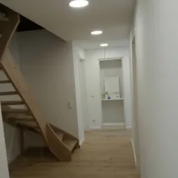 Jasne panele podłogowe w korytarzu z drewnianymi schodami i oświetleniem sufitowym typu downlight.