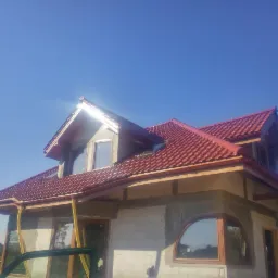 Dom w Brzesku z nowym, czerwonym dachem z dachówki ceramicznej, częściowo jeszcze w trakcie prac wykończeniowych, widoczne okna dachowe.