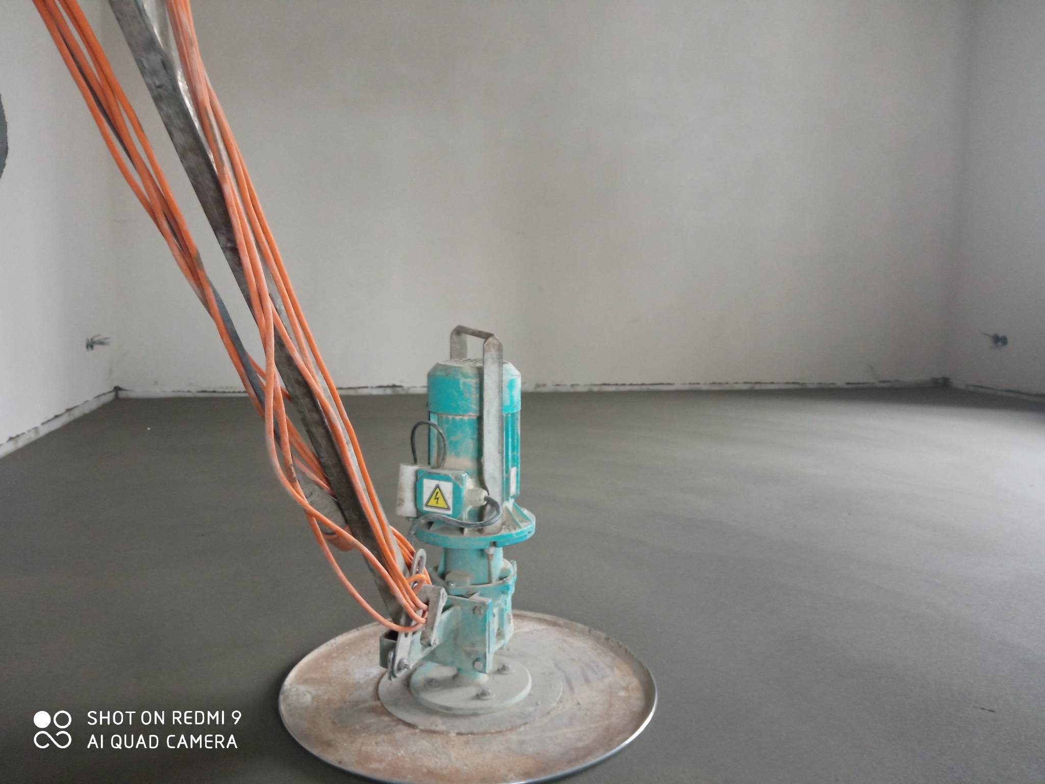 Maszyna do zacierania posadzki jastrychowej na świeżo wylanej powierzchni, widoczne przewody zasilające.