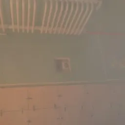 Ściana łazienki w trakcie prac wykończeniowych: widoczne płytki ułożone na podłodze, płyty gipsowo-kartonowe na ścianach z wyciętym otworem na instalację oraz grzejnik drabinkowy pod sufitem.