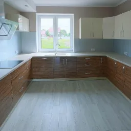 Nowoczesna kuchnia w kształcie litery U z drewnopodobnymi frontami szafek dolnych i jasnymi szafkami górnymi, z dużym oknem z widokiem na ogród.