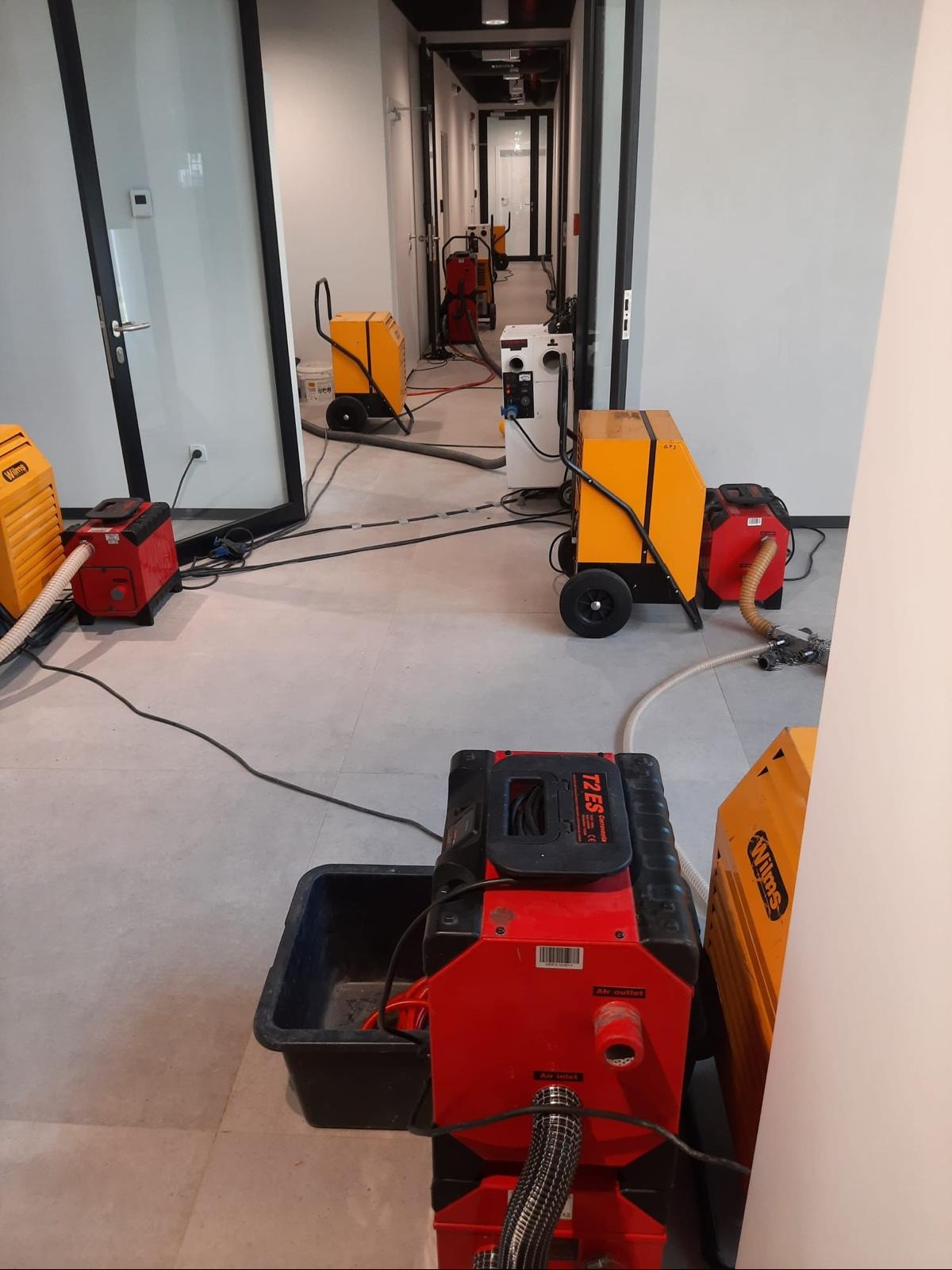 Osuszanie po zalaniu w biurze w Sosnowcu. Widoczne profesjonalne osuszacze powietrza, rozmieszczone wzdłuż korytarza, gotowe do pracy. Sprzęt marki Wilms.