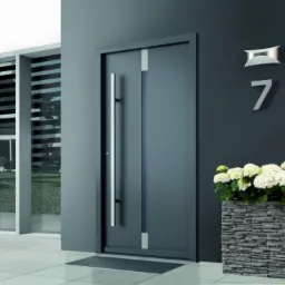 Nowoczesne, szare wejściowe z długim, pionowym uchwytem, numer domu '7' i donica z białymi kwiatami.