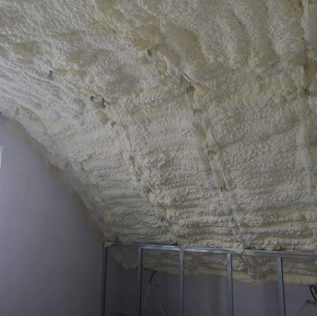 Poddasze pokryte grubą warstwą jasnej pianki izolacyjnej, widoczne metalowe profile konstrukcyjne ścianki działowej w dolnej części kadru.