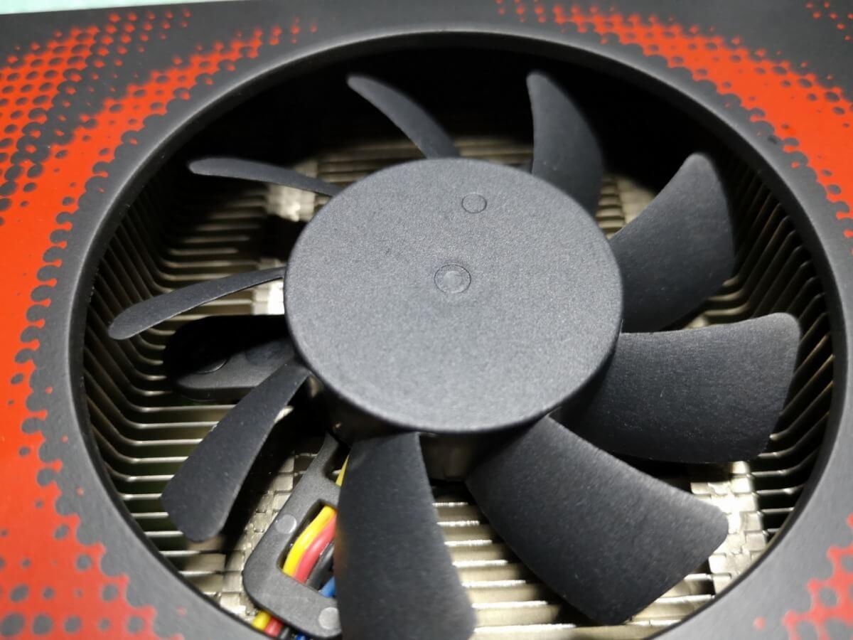 Czarny wentylator karty graficznej z czerwonymi akcentami, widoczne żeberka chłodzące i kolorowe przewody.