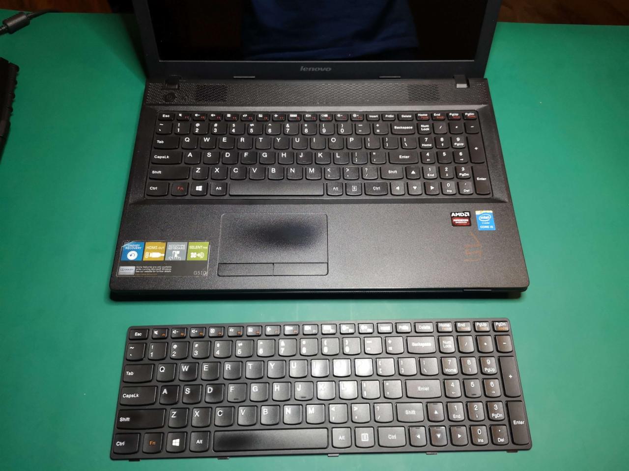 Otwarty laptop Lenovo z widoczną klawiaturą i dodatkowa, wymontowana klawiatura obok, na zielonym tle