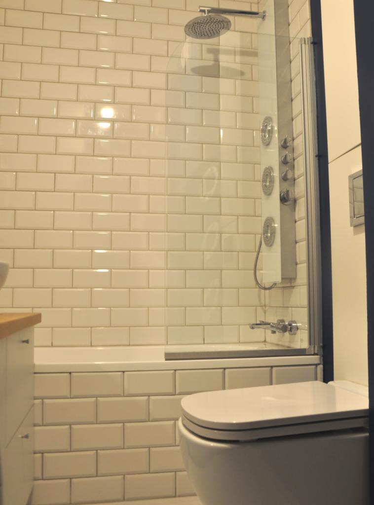 Wykończona łazienka z białą armaturą, kabiną prysznicową z panelem hydromasażu i klasycznymi białymi płytkami typu metro na ścianach.