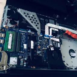 Wnętrze rozłożonego laptopa Dell z widoczną płytą główną, pamięcią RAM, wentylatorem i dyskiem twardym, obok leżą małe śrubki i czerwony śrubokręt.