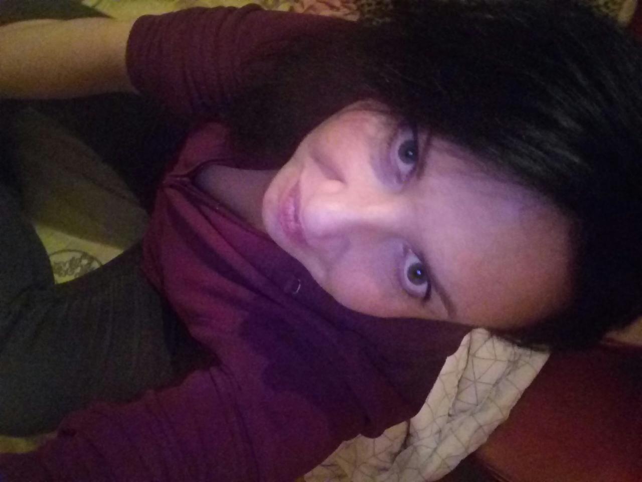 Portret kobiety z ciemnymi włosami, patrzącej w górę, z bliska, w bordowej bluzce, na tle wzorzystej powierzchni.