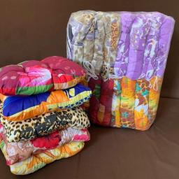 Mikolajczyk - Stos poduszek na krzesła w kwiatowe i zwierzęce wzory, część zapakowana w folię, na brązowej sofie.