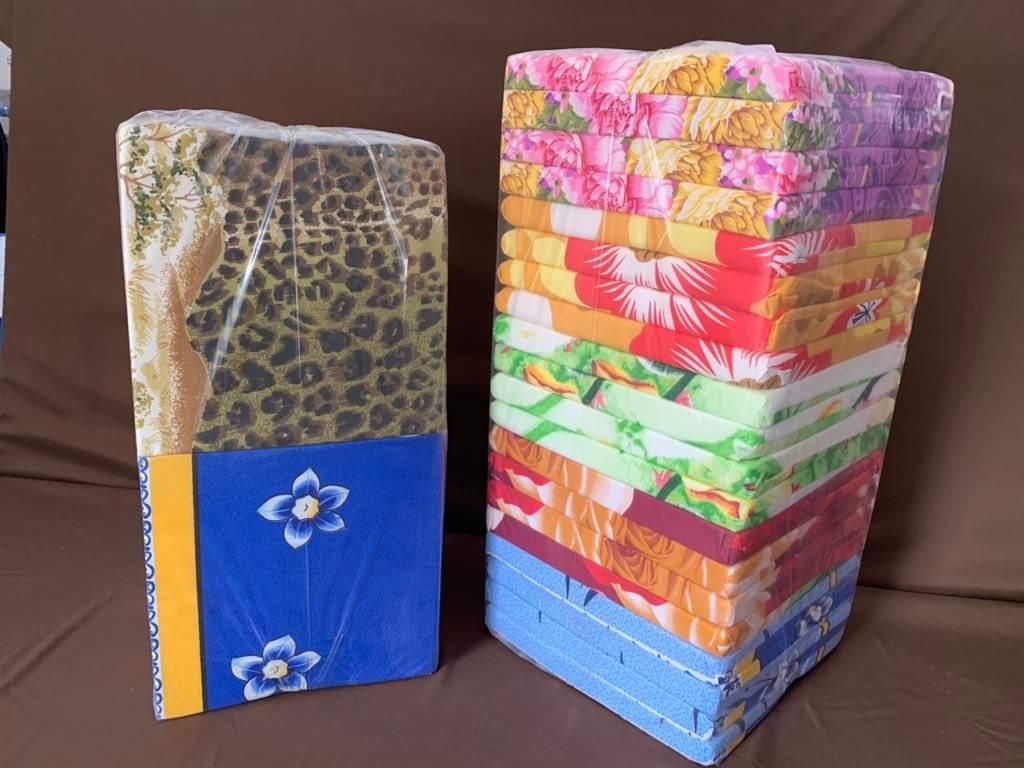 Dwa stosy kolorowych, zapakowanych w folię poduszek na krzesła. Jeden stos z motywem zwierzęcym i kwiatowym, drugi z różnorodnymi wzorami kwiatowymi i geometrycznymi.