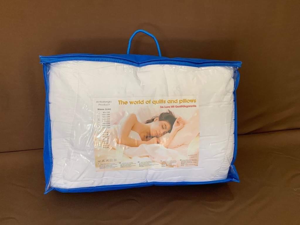 Antyalergiczna poduszka w przezroczystym, niebieskim opakowaniu z uchwytem, z widoczną etykietą prezentującą zdjęcie śpiącej kobiety oraz informacje o rozmiarach.