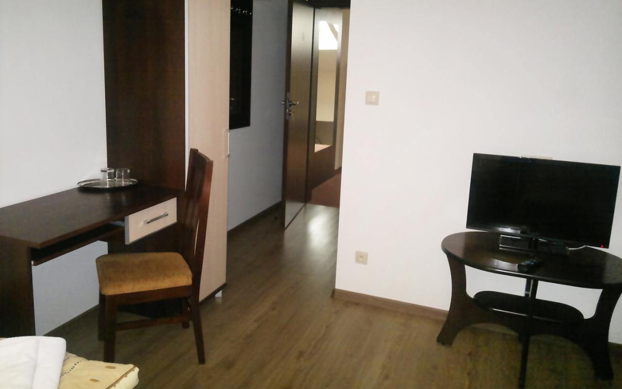 Pokój hotelowy z biurkiem, krzesłem, telewizorem i otwartymi drzwiami do kolejnego pomieszczenia.