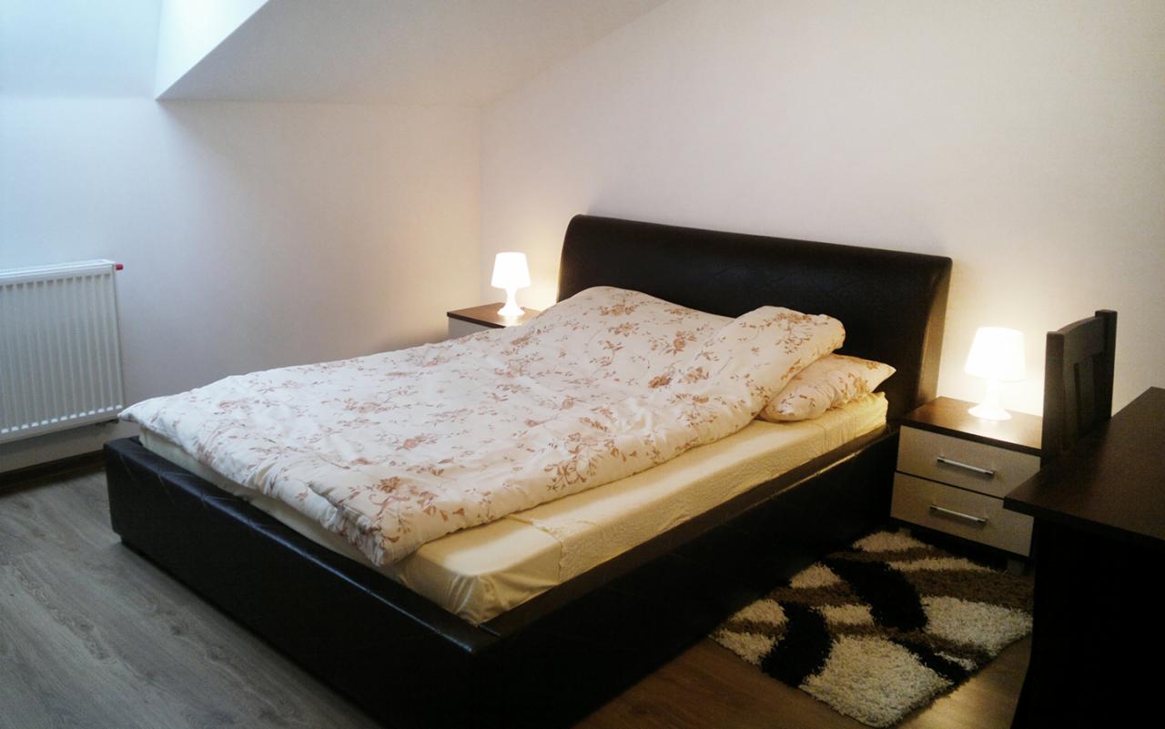 Sypialnia na poddaszu z czarnym łóżkiem, pościelą w kwiaty, grzejnikiem i dywanikiem z wzorem geometrycznym.