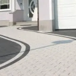 Kaskadowa ścieżka z jasnoszarej kostki brukowej z ciemnoszarymi obrzeżami, prowadząca od domu z białymi kolumnami do białej bramy garażowej.