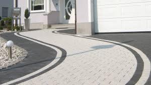 Kaskadowa ścieżka z jasnoszarej kostki brukowej z ciemnoszarymi obrzeżami, prowadząca od domu z białymi kolumnami do białej bramy garażowej.