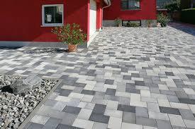 Ułożona z kostki brukowej powierzchnia przed budynkiem z czerwoną elewacją w Wągrowcu. Widoczny fragment obrzeża z drobnymi kamieniami i pojedynczy duży kamień na pierwszym planie.