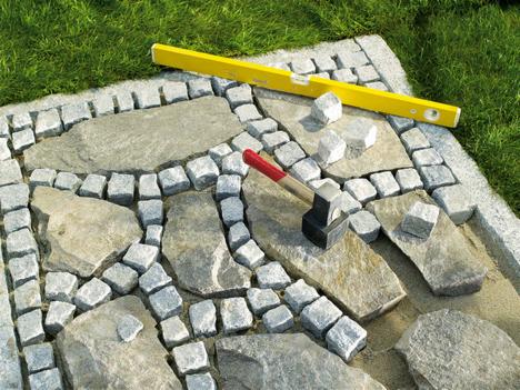 Układanie kamiennej ścieżki w ogrodzie: żółta poziomica, gumowy młotek i kostki brukowe z granitu na podsypce piaskowej.