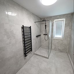 NOVEX Sławomir Nowak - Nowoczesna łazienka z szarymi płytkami, czarną armaturą i grzejnikiem drabinkowym, kabina prysznicowa typu walk-in z odpływem liniowym.