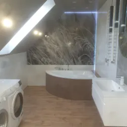 Nowoczesna łazienka na poddaszu z wanną obudowaną drewnopodobną płytką, umywalką z szafką, pralką Electrolux i tapetą z motywem trawy.