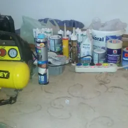 Stanowisko pracy z kompresorem Stanley, przedłużaczem, puszkami farb, gipsu i innymi materiałami budowlanymi na dywanie.