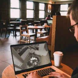 Mężczyzna przegląda na laptopie wizualizację wnętrza kuchni w kawiarni, obok stoi kubek z kawą.