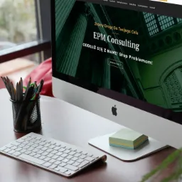 Monitor iMac wyświetlający stronę internetową EPM Consulting na biurku z telefonem, klawiaturą i przyborami do pisania, z widokiem z okna w tle.