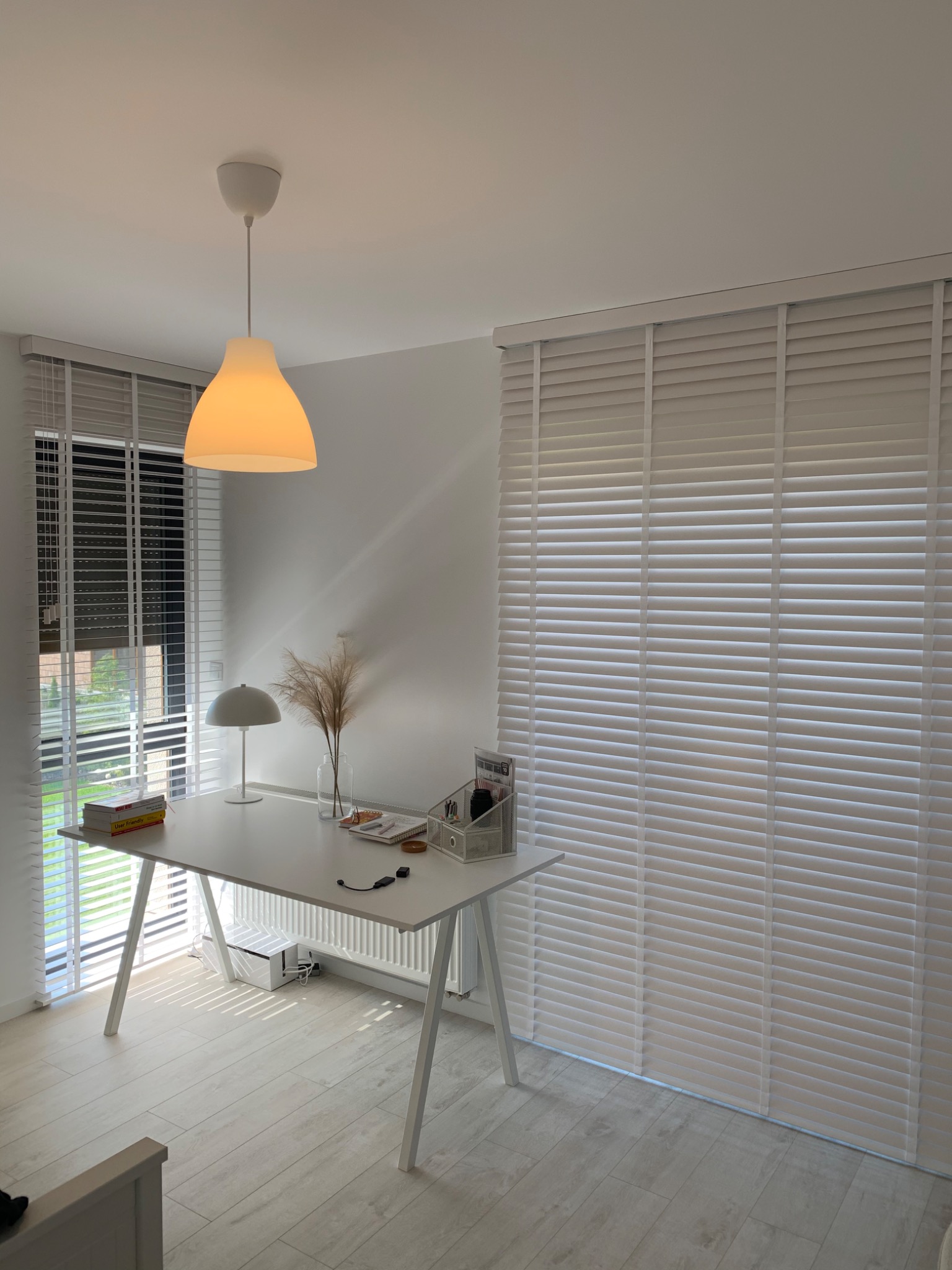 Jasne wnętrze z białym biurkiem i drewnianymi żaluzjami poziomymi w oknach.